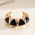 Gros plan sur un bracelet manchette doré avec incrustations géométriques noires - Bracelet Rigide - Large / Or-Noir