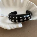 Close-up of a black resin cuff bracelet with silver studs in a white shell dish. - Style 59