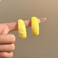 Primer plano detallado de pendientes de aro en C con encaje amarillo puestos en un dedo. - Tops / Amarillo