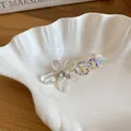 Close-up of transparent flower hair clip with pearls and heart rhinestones in a shell dish. - Duckbill Clip - Single / Transparent Flower (Rhinestone)