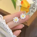 Close-up of dainty white daisy flower stud earrings held between fingers for scale - Daisy (HE33906) / Silver