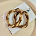 Dettaglio ravvicinato di elastici per capelli intrecciati caffè e beige su un vassoio - Marrone Scuro e Cachi Misto