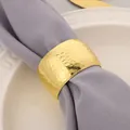 Close-up detail of a luxury golden hammered metal napkin ring on a grey cloth napkin - Honeycomb Hammered Style / Gold