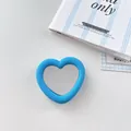 Detailed view of a blue heart-shaped silicone mirror phone grip on a white surface. - Dark Blue