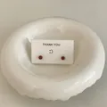 Nahaufnahme minimalistischer brauner Kugelohrringe auf einer weißen Dankeskarte in einer Schale. - Braun