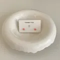 Nahaufnahme von rosa Mini-Ohrsteckern in Bonbonform auf einer weißen „Thank You“-Karte. - Rosa