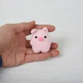 Cute handmade pink crochet pig keychain held in hand on a white background for scale - Pig