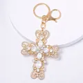Primo piano dettagliato di un portachiavi a croce dorata con brillanti strass - Cuore e Croce / Bianco