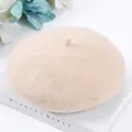 Detailed view of a soft beige wool beret hat resting on a decorative white book - One Size / Beige