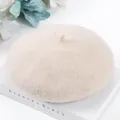 Detailed macro view of a soft beige wool beret hat placed on a decorative white book - One Size / Cream