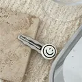 Silver wavy duckbill hair clip with white smiley face icon on textured background - Lacquered Smiley Face Wavy Clip (J8.4) / Off White