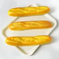 Drei realistische Baguette-Quetschspielzeuge auf einem minimalistischen cremefarbenen Tablett - Baguette 26cm