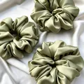 Set of three oversized sage green satin scrunchies displayed on elegant draped silk - Grass Green