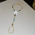 Detalle de una pulsera de mano dorada con flor de esmalte blanco y pedrería de colores - Cadena de mano / Plateado-Blanco-Multicolor
