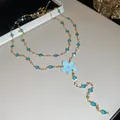 Detalle de un collar dorado con colgante de flor azul y pedrería brillante. - Collar / Dorado-Azul