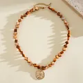 Dettaglio di una collana di perline di conchiglia marrone con ciondolo a moneta d'oro ritratto - Choker Necklace / Oro-Marrone