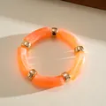 Detail view of orange marbled acrylic cylindrical beads with gold metal spacers on a bracelet. - Bracelet / Orange