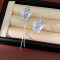 Detailed view of asymmetrical blue butterfly earrings with long silver tassels. - Clip-On Earrings / Silver-Blue