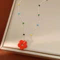 Vue détaillée d'un collier avec pendentif fleur en verre coloré et chaîne à billes argentée. - Rouge