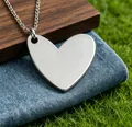 Close-up view of minimalist stainless steel heart-shaped pendant on denim and grass - Steel