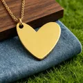 Detailed close-up of a minimalist polished gold heart pendant necklace on blue denim background - Gold