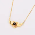 Detail view of an 18k gold angel wings necklace with a heart-shaped projection stone. - Gold