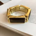 Macro detail of a vintage gold-toned rectangular resin stretch bracelet resting on a book - Pink