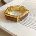 Dettaglio del bracciale elastico vintage in resina dorata con maglie rettangolari su libro. - Marrone