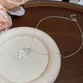 Elegant close-up of zircon flower and mint green enamel bow pendant on a silver necklace chain - Silver Style (White Bow)