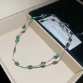 Close-up detail van een minimalistische zilverkleurige ketting met levendige groene ovale stenen - Ketting / Zilver-Groen