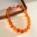 Close-up detail of translucent amber acrylic beaded necklace on a wooden tray surface - Amber Round Bead Necklace (42#) / Gold Brown