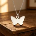 Detailopname van een minimalistische zilveren vlinderhanger met spiegelafwerking - Vlinder Hanger Ketting (Staal Kleur)