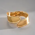 Nahaufnahme eines goldfarbenen, unregelmäßigen geometrischen Kreuz-Armreifs - Unregelmäßiger Kreuzstil / Gold