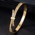 Dettaglio di un bracciale rigido in acciaio dorato a forma di fiocco con zirconi. - Oro Zircone Bianco