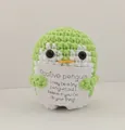 Detailed close-up of a green handmade crochet penguin holding a card with positive message - Penguin / Green