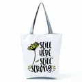 Front detail of white tote bag with sunflower and 'STILL HERE STILL STRONG' print - Sunflower Dragonfly Slogan (hl5319)
