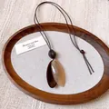 Macro detail of irregular oval pendant on retro brown wax cord necklace - Oval (HN9947)