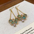 Close-up of vintage butterfly dangle earrings with iridescent green and pink glass drops - Gold-Green