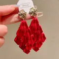 Close-up shot of elegant red petal tassel drop earrings with gold studs held by hand - Red