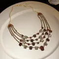 Close-up of multi-layer vintage necklace with amber and clear crystals on white plate - Necklace / Gold Brown