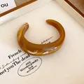 Primo piano di un bracciale rigido aperto in resina marmorizzata ambra su vassoio - Caffè Scuro