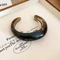 Primo piano di un bracciale rigido in resina marmorizzata con finitura tartarugata liscia. - Nero