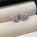 Elegant macro view of purple heart-shaped stud earrings featuring silver bowknot accents - Purple