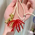 Detailed close-up of a golden horse pendant necklace featuring vibrant red beaded tassels. - Bright Gold