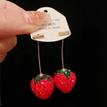 Macro view of sparkly rhinestone-encrusted strawberry dangle earrings on display card - Strawberry / Red