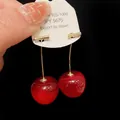 Close-up detail of realistic red cherry earrings hanging from a white product tag - Cherry / Red