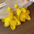 Dettaglio di orecchini a fiore in chiffon giallo vibrante con borchie in rafia - Giallo