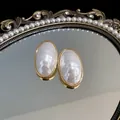 Close-up of elegant oval pearl earrings with gold-plated finish on a decorative mirror. - White (Silver Post Gold Plated)