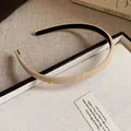 Detailed macro view of a beige flocked fabric thin headband featuring a golden 'Love' metal tag. - Beige