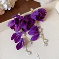 Dettaglio di orecchini a fiore in tessuto viola con perle e cristalli su un vassoio. - Viola